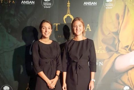 Two women at a promotional event backdrop.